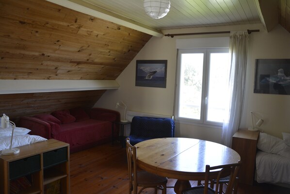 A cozy room with a wooden ceiling, a round table, a red sofa, and a blue armchair. - Breathtaking view of Omaha Beach. For vacations with family and friends! (Vierville-sur-Mer)