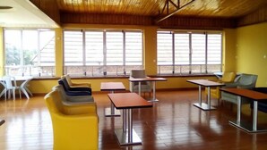 Ein geräumiges Zimmer mit Holzboden, großen Fenstern und modernen Möbeln, darunter Stühle und Tische.