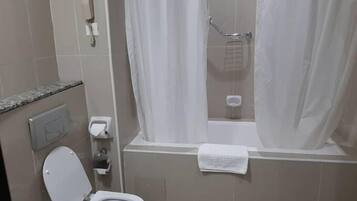 A bathroom with a toilet, a shower with a curtain, a towel hanging on the wall, and a hand dryer.