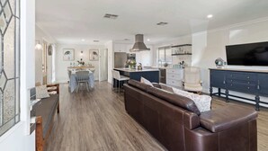 Eine moderne Küche mit einer zentralen Kochinsel, einem Essbereich mit Tisch und Stühlen, einem braunen Ledersofa und einem an der Wand montierten Fernseher.