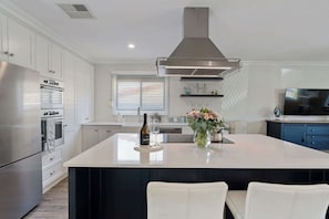 A modern kitchen with stainless steel appliances, a central island, and a large overhead vent. - Rose Cottage 3B Hutchinson St Goolwa (Goolwa)