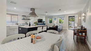 Eine moderne Küche mit Kochinsel, Essbereich mit gemustertem Tischlein und Wohnbereich mit Sofa und Sesseln.
