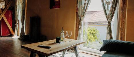 A cozy living room with a wooden table, a sofa, and a window with curtains.