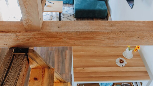 A wooden staircase leading to a lofted area with a view of a green couch and a small table with a flower vase. - Vacation apartment Linda (Ilmenau)