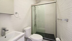 A modern bathroom with a glass-enclosed shower, a white toilet, and a sink with a marble countertop. - Prime soho 2 bedroom (New York)