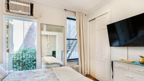 Ein Schlafzimmer mit Bett, Schminktisch, Fernseher und einem Fenster mit Blick auf Grünflächen.
