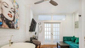 Ein Zimmer mit einem runden Esstisch, einem grünen Sofa, einem Deckenventilator und einem großen Fenster.