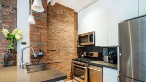 Une cuisine moderne avec un mur en briques, des appareils électroménagers en acier inoxydable et des meubles blancs.
