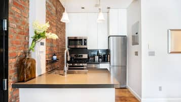 Una cocina moderna con pared de ladrillo decorativa, electrodomésticos de acero inoxidable e iluminación colgante.