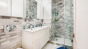 Une salle de bain moderne avec une douche à l’italienne en verre, un meuble-lavabo blanc avec un miroir et un pare-feu en carreaux.