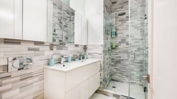 Un baño moderno con cabina de ducha de vidrio, tocador blanco con espejo y salpicadero de azulejos.
