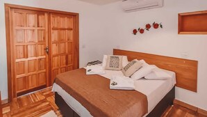 Une chambre avec un lit en bois, une grande armoire en bois, un ventilateur de plafond et un climatiseur fixé au mur.