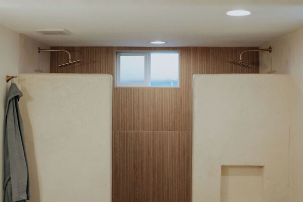 Baño con dos cabinas de ducha, paredes de paneles de madera y un ventanal pequeño.