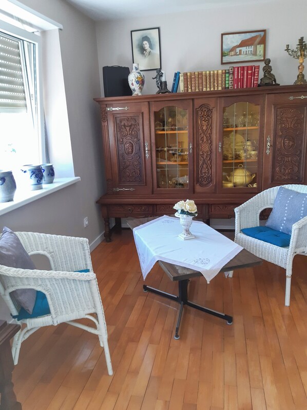 A room with a wooden cabinet, two white wicker chairs, a small table with a white tablecloth, and a window with blinds. - Rest in the shade of the Sequoia, in the Vosges du Nord Regional Nature Park (Enchenberg)