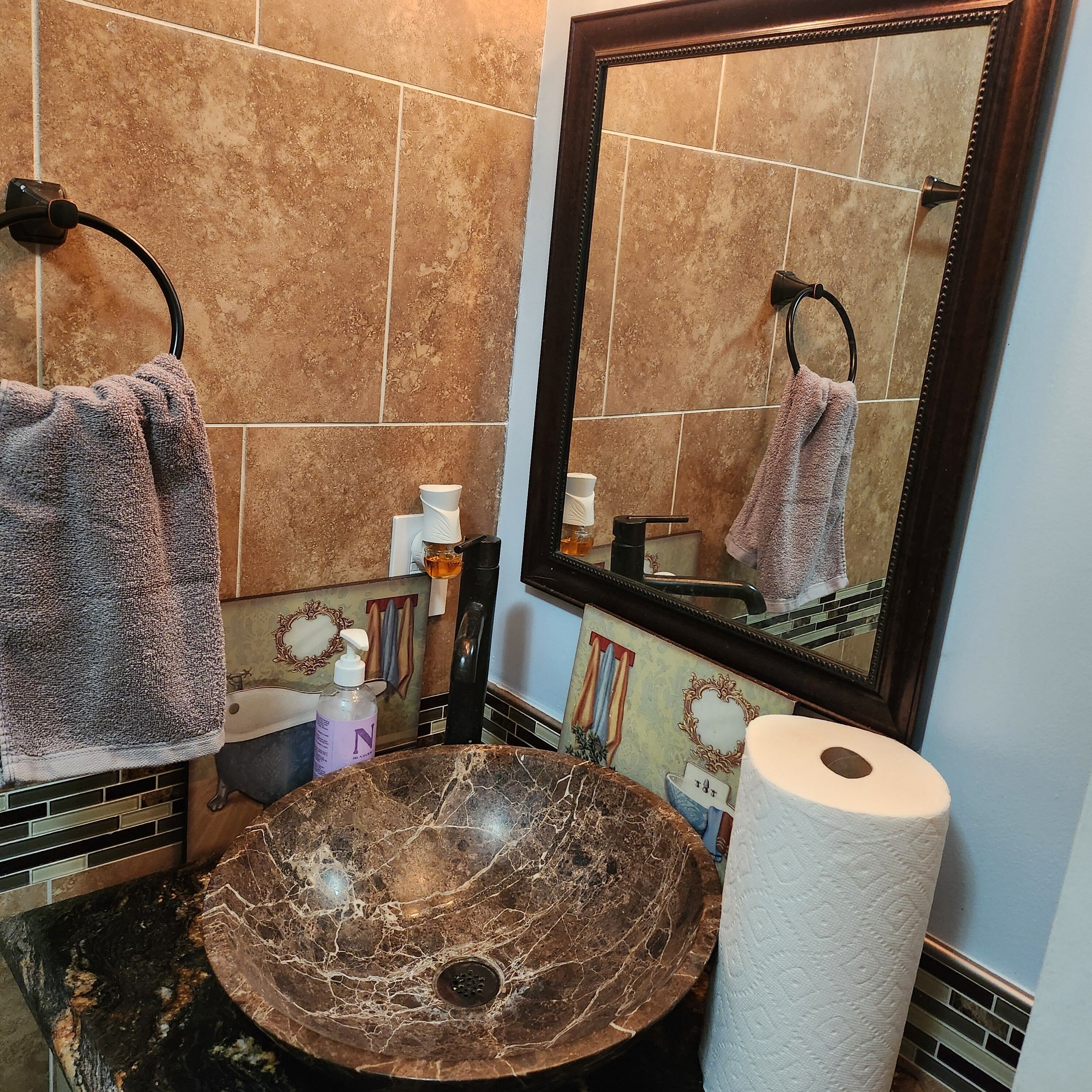 Un baño con lavamanos de mármol, un espejo grande y dos toallas colgadas en ganchos.