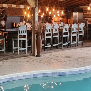 Un área junto a la piscina con una fila de sillas blancas y un jarrón grande.