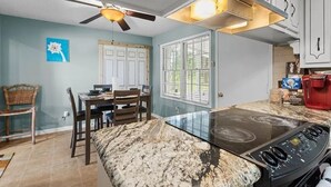 Une cuisine équipée d’une cuisinière à gaz, d’un ventilateur de plafond et d’un coin repas avec une table et des chaises.