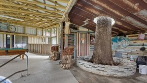 Un espace piscine intérieur au style rustique, avec un plafond en bois, une sculpture d’arbre au centre et une table de billard.