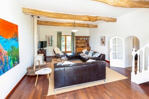 A spacious living room with a large black leather sofa, a wooden bookshelf, and a painting on the wall.