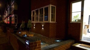 Una vista notturna di un edificio con una finestra, un muro in mattoni e un piccolo giardino con un vialetto.