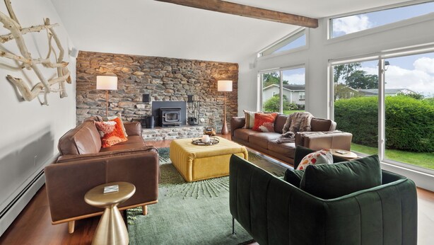 A modern living room with a stone wall, fireplace, leather sofas, and a large window offering a view of the outdoors.