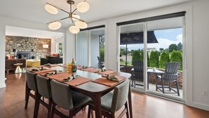 A dining area with a large table, chairs, and a modern chandelier. There is a stone wall and a fireplace in the background.