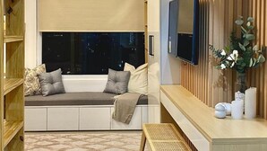 Un saló modern amb una zona d'estar integrada, un televisor de pantalla plana fixat a una paret de fusta i una finestra gran amb vista a la ciutat de nit.