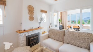 A modern living room with a fireplace, a sofa, and a dining area with a view of the outdoors.