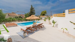 A pool area with lounge chairs, a table, and a thatched umbrella.
