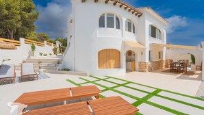A white villa with a patio, outdoor furniture, and a stone wall.