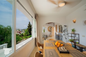 A dining area with a large window, a wooden table, and a bowl of oranges.