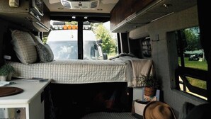 Interior d'una caravana compacta amb lliteres, cuina americana i zona de menjador petita.