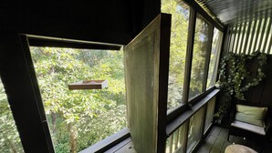 A room with large windows, a wooden bench, and a hanging planter. - Forest Getaway & Golf at Lake (Bloomington)