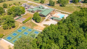 An aerial view of a large property with multiple tennis courts, a swimming pool, and a building with a green roof. - Forest Getaway & Golf at Lake (Bloomington)