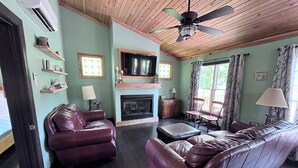 A living room with a fireplace, leather sofas, a television, and a ceiling fan.