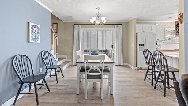 Un coin repas avec une table et des chaises, un lustre et une vue sur la cuisine.