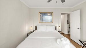 Une chambre d’hôtel avec un grand lit, un ventilateur de plafond, un tableau encadré au mur et une porte donnant sur la salle de bain.