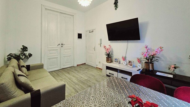 A living room with a sofa, a dining table, and a TV mounted on the wall. - Modern & comfy oasis in city.  (Anderlecht)