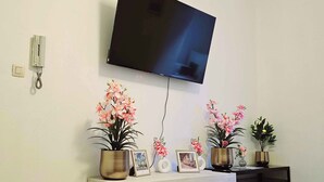 A living room with a TV mounted on the wall, a wooden entertainment unit with decorative plants, and a wall-mounted telephone. - Modern & comfy oasis in city.  (Anderlecht)