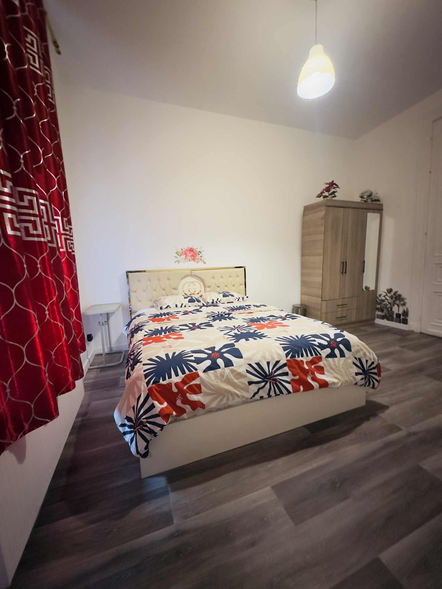 A bedroom with a bed, a wardrobe, a nightstand, and a hanging light fixture.