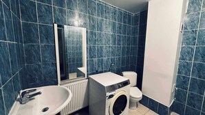 A bathroom with blue tiles, a sink, a washing machine, and a toilet. - Modern & comfy oasis in city.  (Anderlecht)