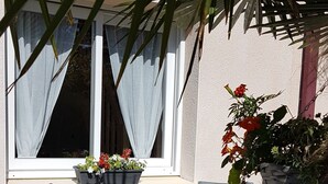 An outdoor seating area with two chairs and a table, a window with curtains, and potted plants.