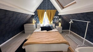 Un dormitorio con cama, mesitas de noche, lámpara y ventana con cortinas.