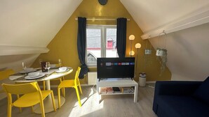 Un comedor con una mesa dispuesta para dos personas, un televisor y una estantería con libros.