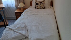 Un lit simple avec une tête de lit en bois, une table de chevet avec une lampe et une fenêtre avec des rideaux.