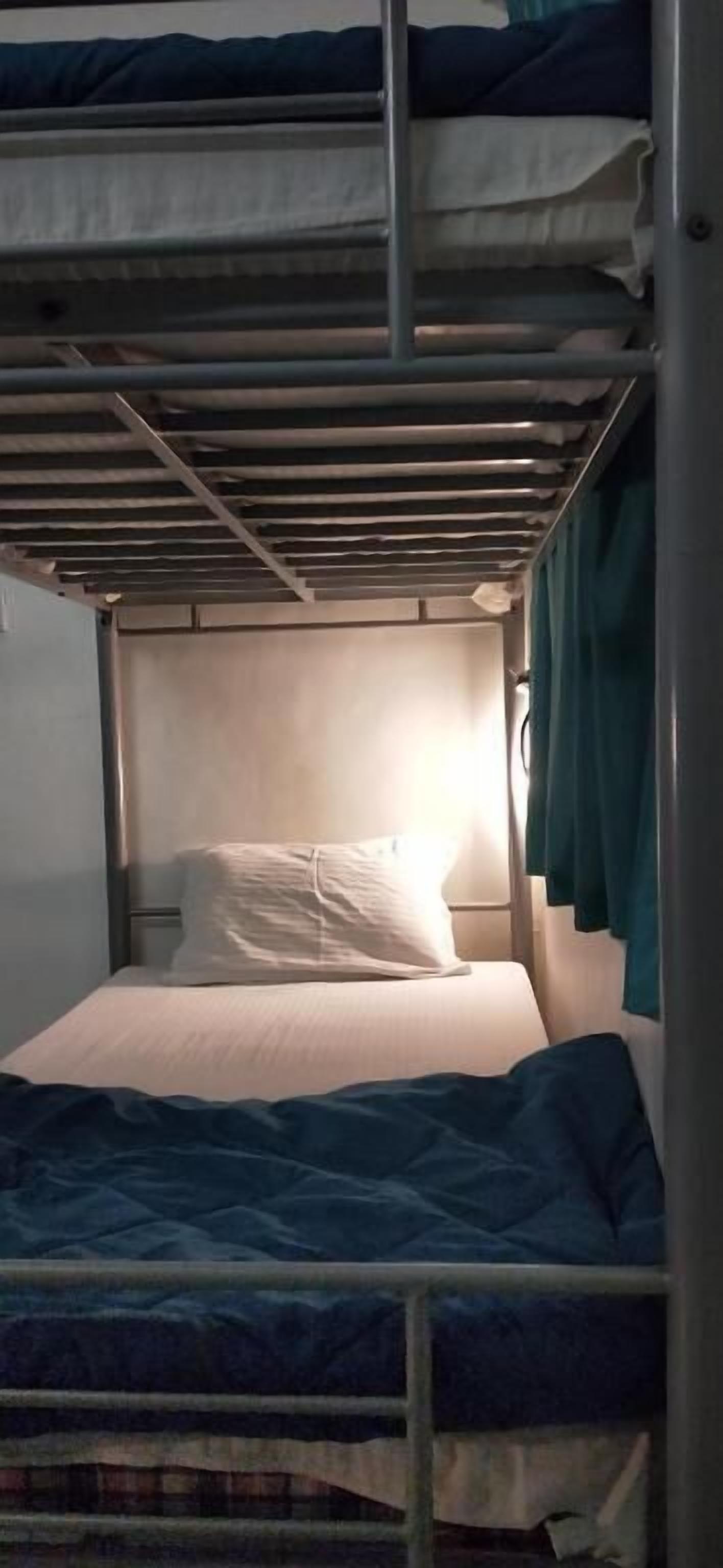 A bunk bed with a headboard, a single bed below, and a curtain on the right side.