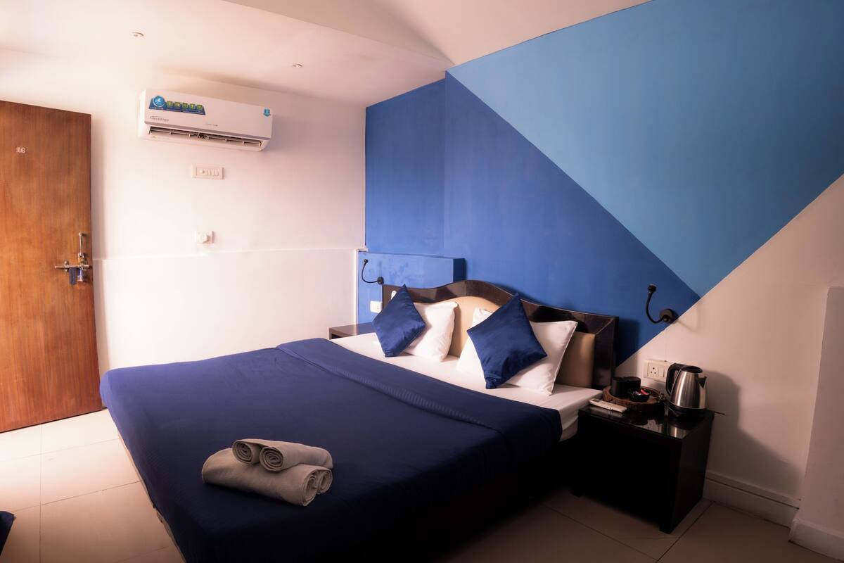 A modern hotel room with a large bed, a nightstand, a coffee maker, and an air conditioning unit.