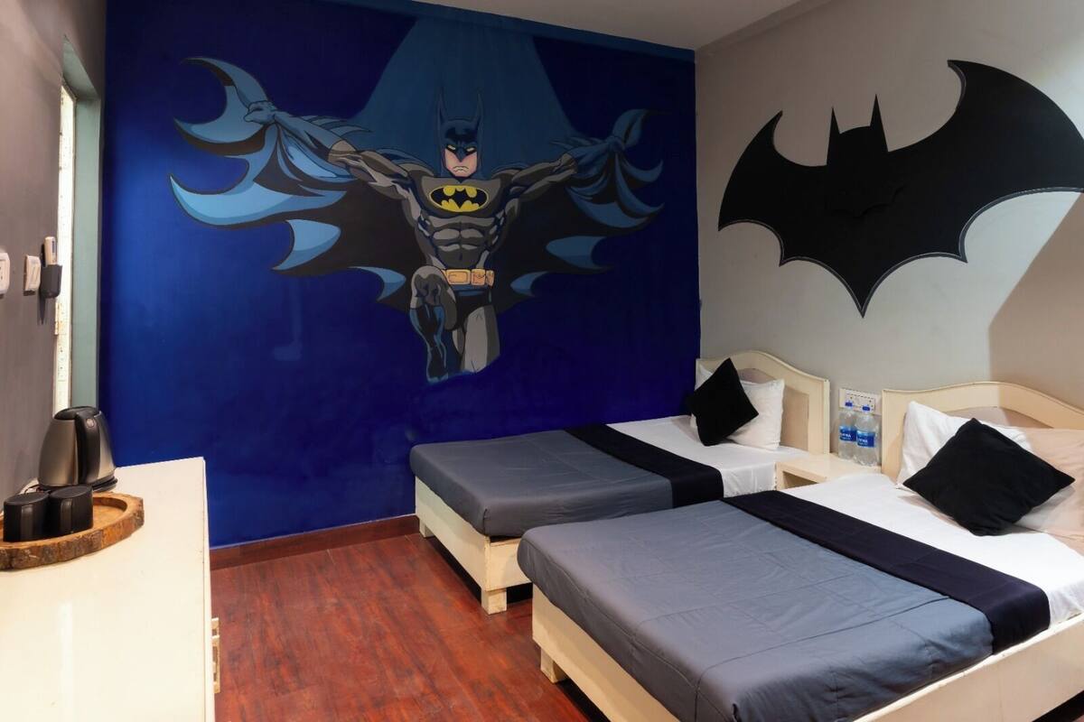 A hotel room with two beds, a large Batman mural, and a water dispenser.