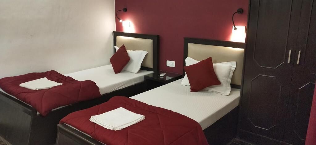 A hotel room with two single beds, each with a red bedspread and white pillows. There are bedside tables with lamps and a dark wooden wardrobe.
