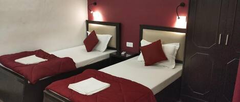 A hotel room with two single beds, each with a red bedspread and white pillows. There are bedside tables with lamps and a dark wooden wardrobe.